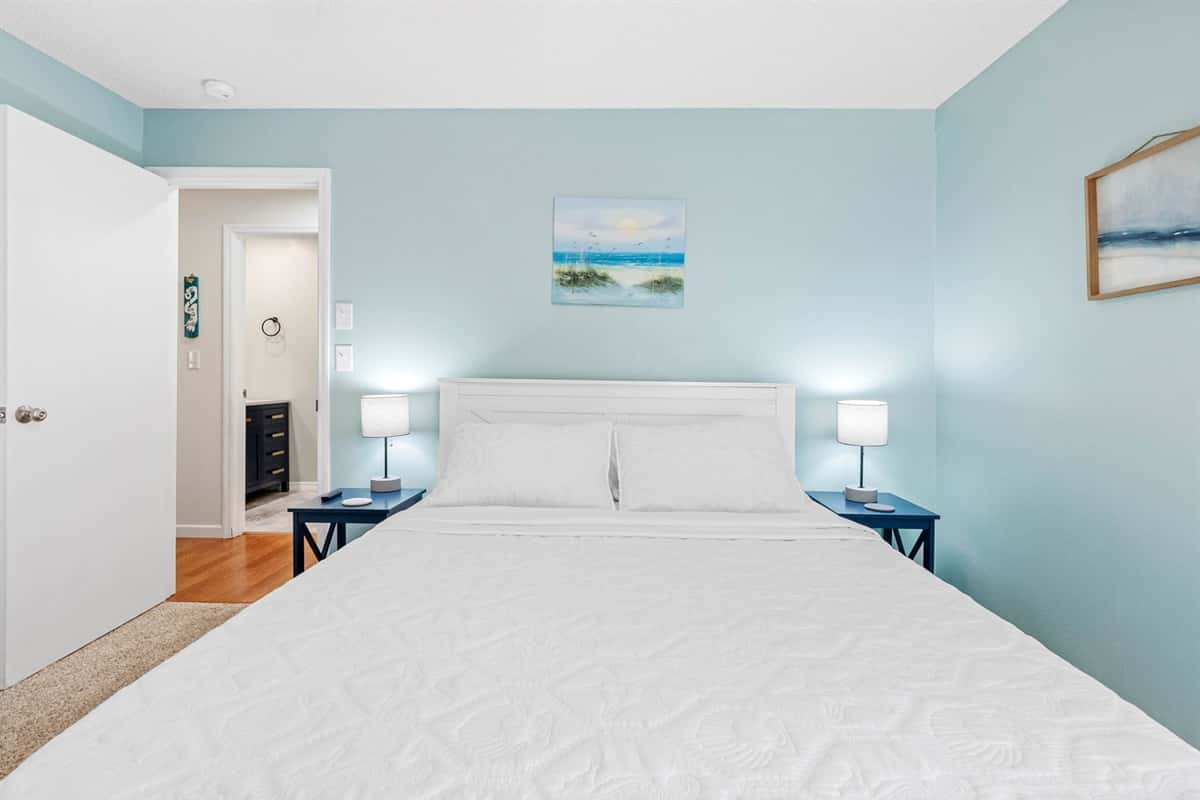 The walls are painted a cool, serene coral blue, evoking the calm and refreshing vibes of the nearby ocean, and are perfectly complemented by the fresh, crisp white linens that dress the bed. 