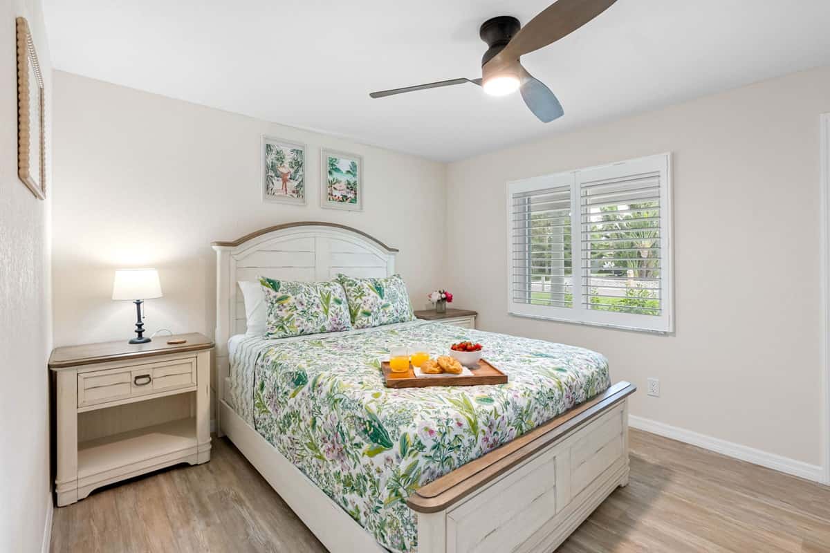 This charming bedroom features a queen bed with soft botanical bedding, a smart TV, and warm wood furnishings for a restful night’s sleep.