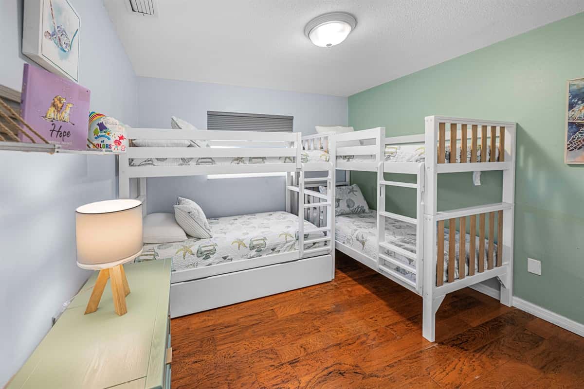 This playful and stylish bedroom is designed to accommodate families or groups, with ample space and a charming decor, wiith two sturdy bunk beds + trundle, offering a mix of white and light wood finishes.