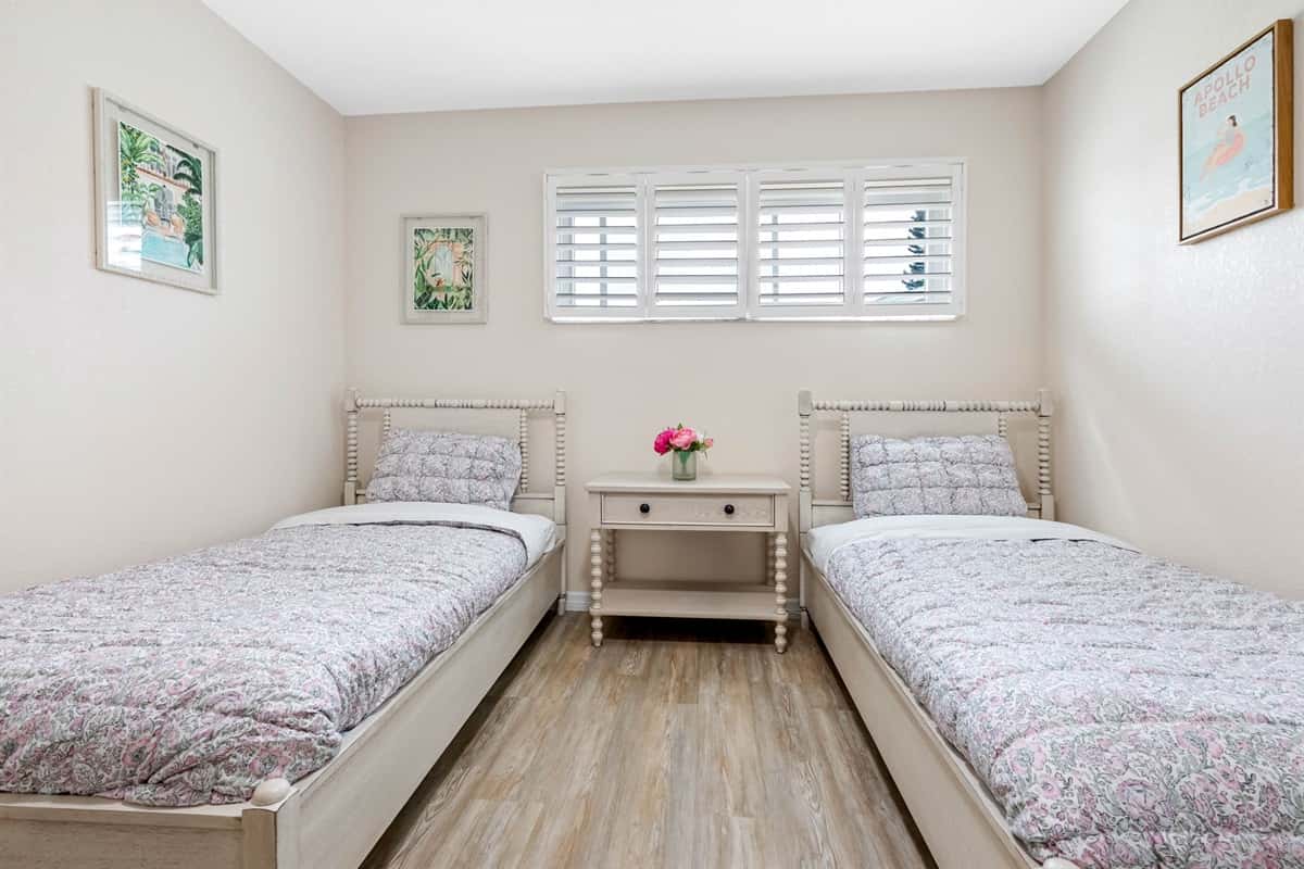 This cozy bedroom features two matching twin beds with light wood frames, a central nightstand with fresh flowers, and cheerful wall art that adds a pop of color.