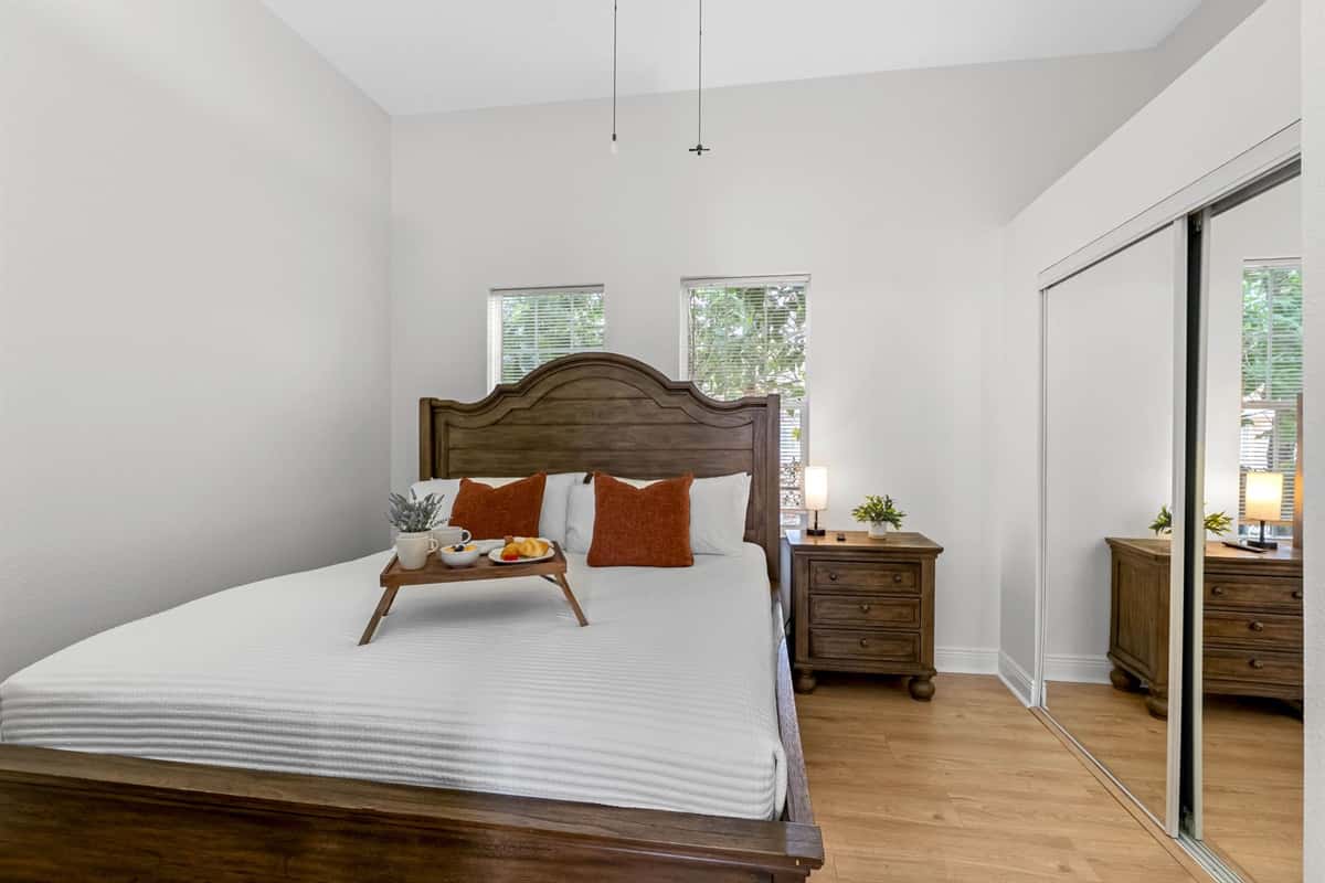 Relax in this inviting bedroom featuring a warm wood bed frame, crisp white linens, and soft accent pillows, creating a calm and comfortable retreat.