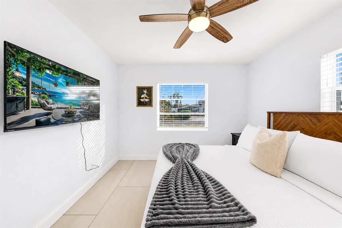 Bedroom 2 featuring a cozy queen bed, wall-mounted TV, and bright natural lighting.