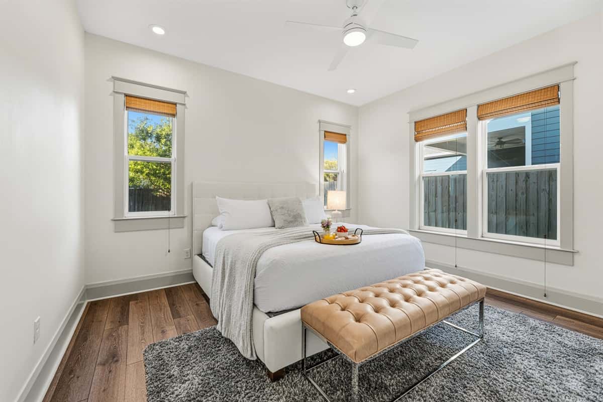 Bright and airy bedroom with a plush bed, tufted caramel bench, ceiling fan, and oversized windows with bamboo shades. All-new finishes and hardwood floors throughout this gorgeous Seminole Heights retreat.