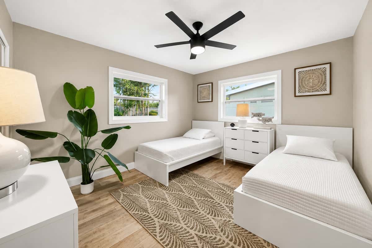Guest bedroom with two twin beds, neutral décor, ceiling fan, and a dresser positioned between the beds.