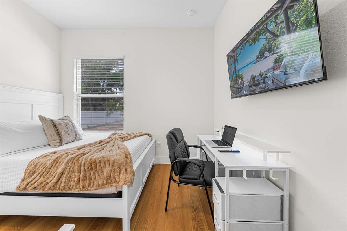 Bright bedroom with comfortable bed, wall-mounted TV, and dedicated workspace.
