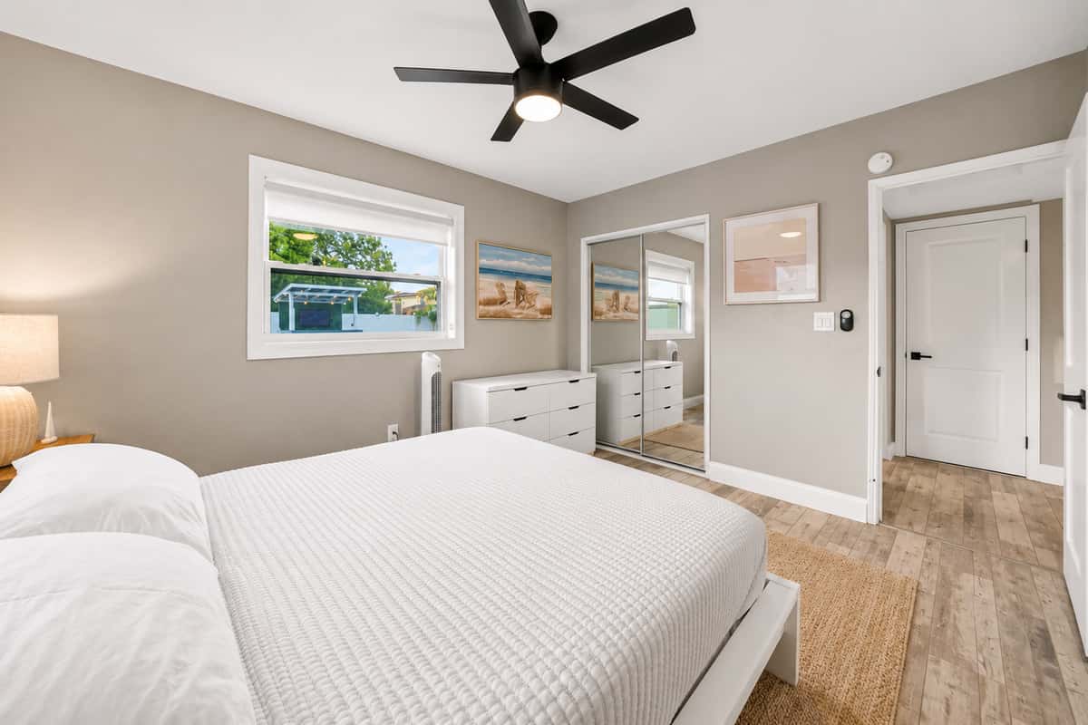 Elegant bedroom view featuring a queen-size bed, ceiling fan, dresser, and private bathroom entrance.