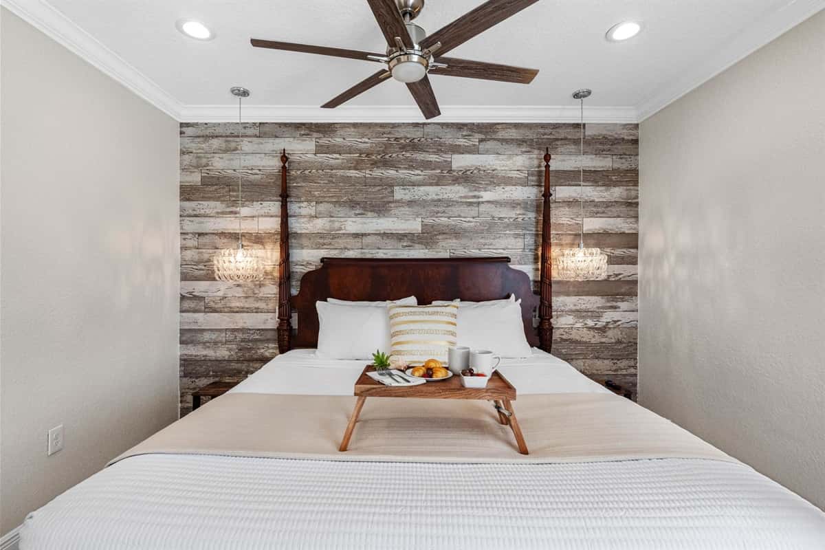 The wood-paneled accent wall and rich four-poster bed bring warmth and character, complemented by neutral tones and polished tile floors.