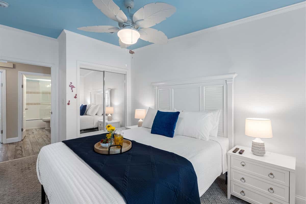 This bright and inviting bedroom features a queen bed with crisp white linens and a calming navy accent blanket.