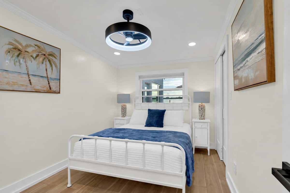 Crisp linens in a breezy queen room. A queen bed with a white metal frame, soft blue bedding and beach art. Simple, fresh and calm, perfect for a couple to recharge.