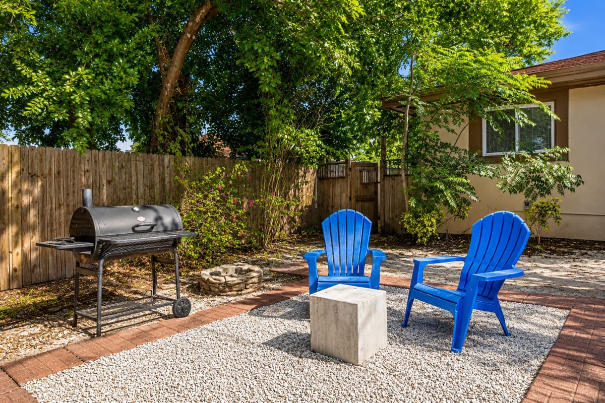 Cozy backyard seating area with Adirondack chairs, charcoal grill, and peaceful garden surroundings.
