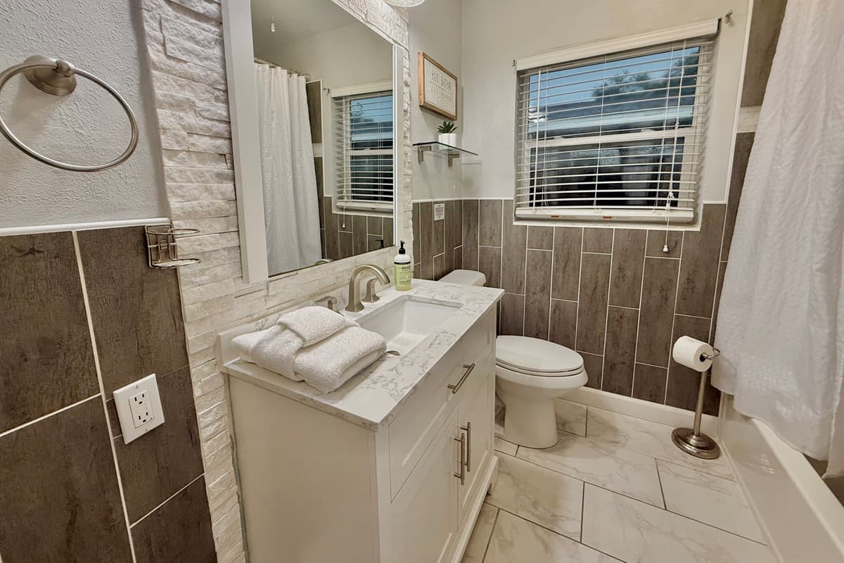 This freshly updated bathroom boasts chic tile design, a bright vanity with marble top, and a deep soaking tub with shower.