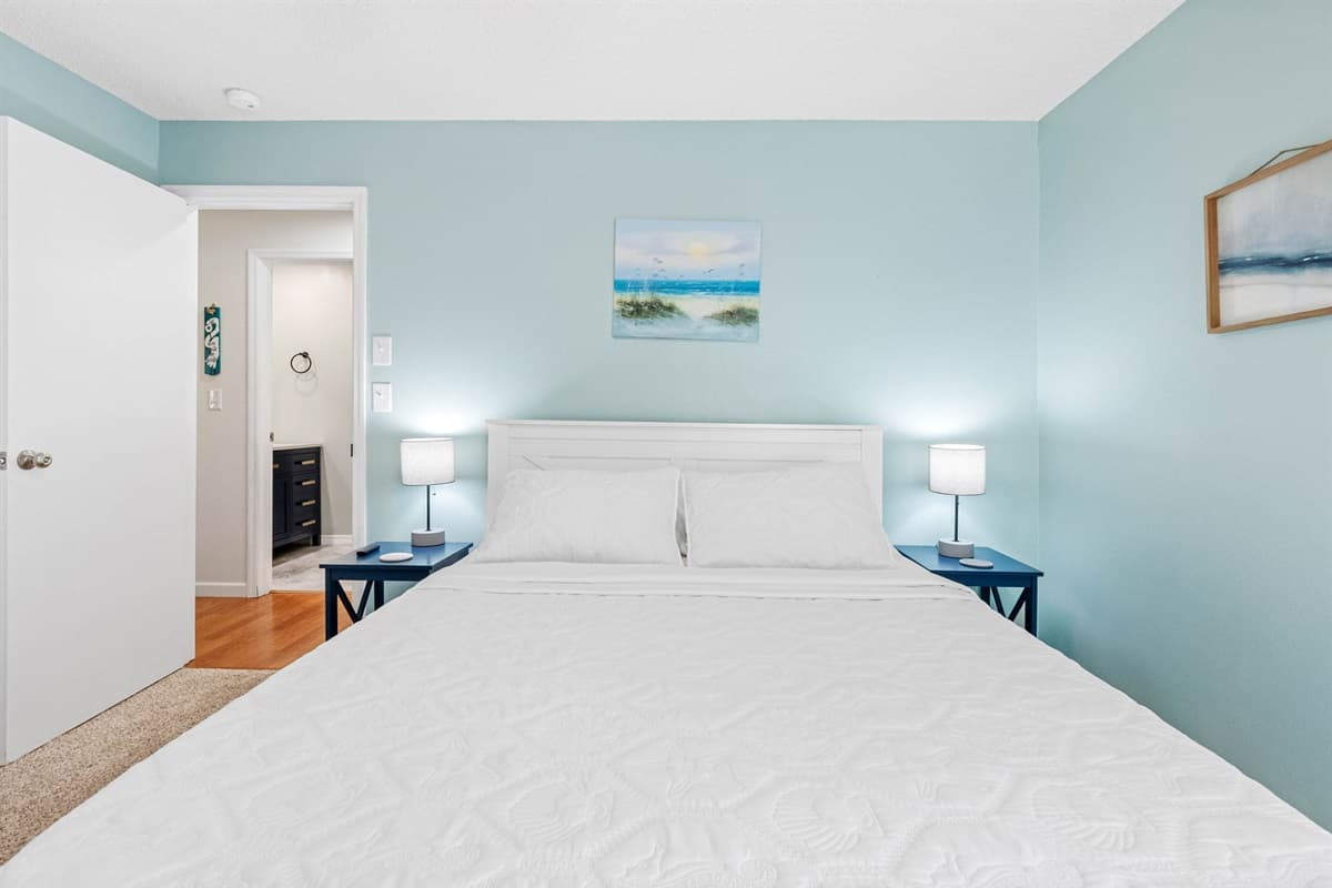The walls are painted a cool, serene coral blue, evoking the calm and refreshing vibes of the nearby ocean, and are perfectly complemented by the fresh, crisp white linens that dress the bed. 