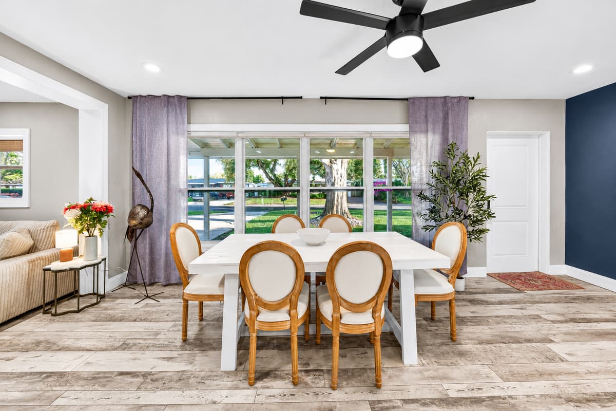 Elegant dining area with seating for multiple guests, large windows overlooking the yard, and soft coastal color accents.