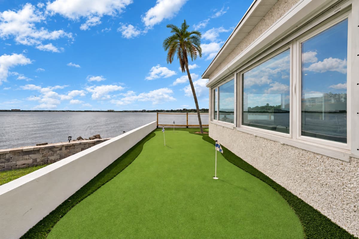Narrow green, big water view. The putting green runs between the house and the bay. Every shot comes with a view of open water and palm trees.