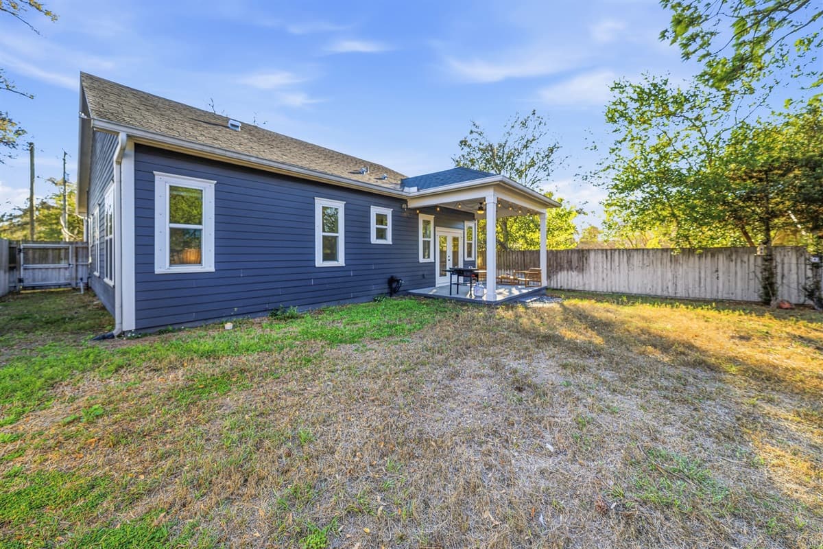 The rear exterior of this brand-new Seminole Heights home showcases clean modern lines, fresh charcoal board-and-batten siding, and a generous fully fenced backyard with endless potential for outdoor fun under Tampa's sunny skies.