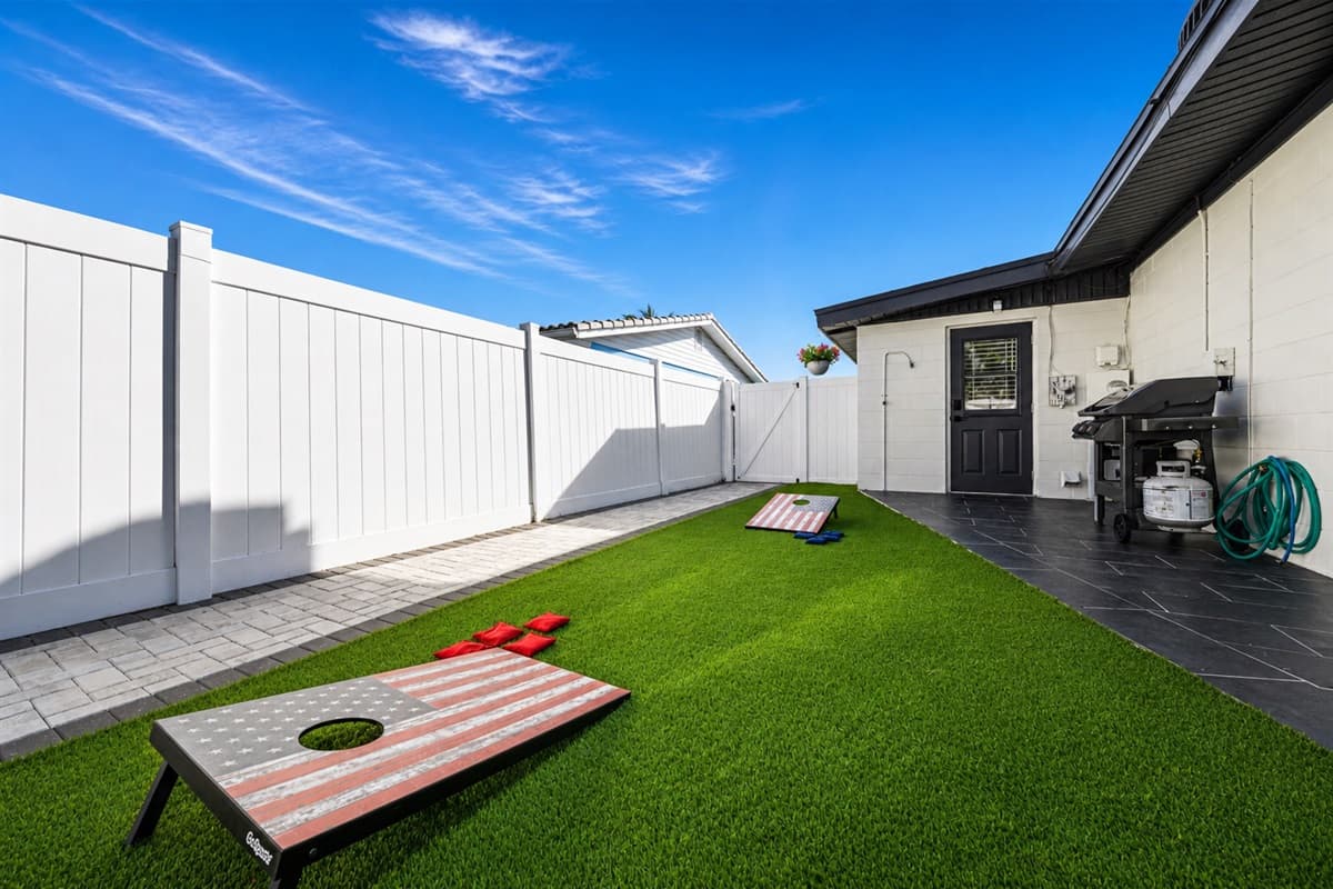 Backyard recreation space featuring cornhole boards, grill area, and spacious turf lawn.