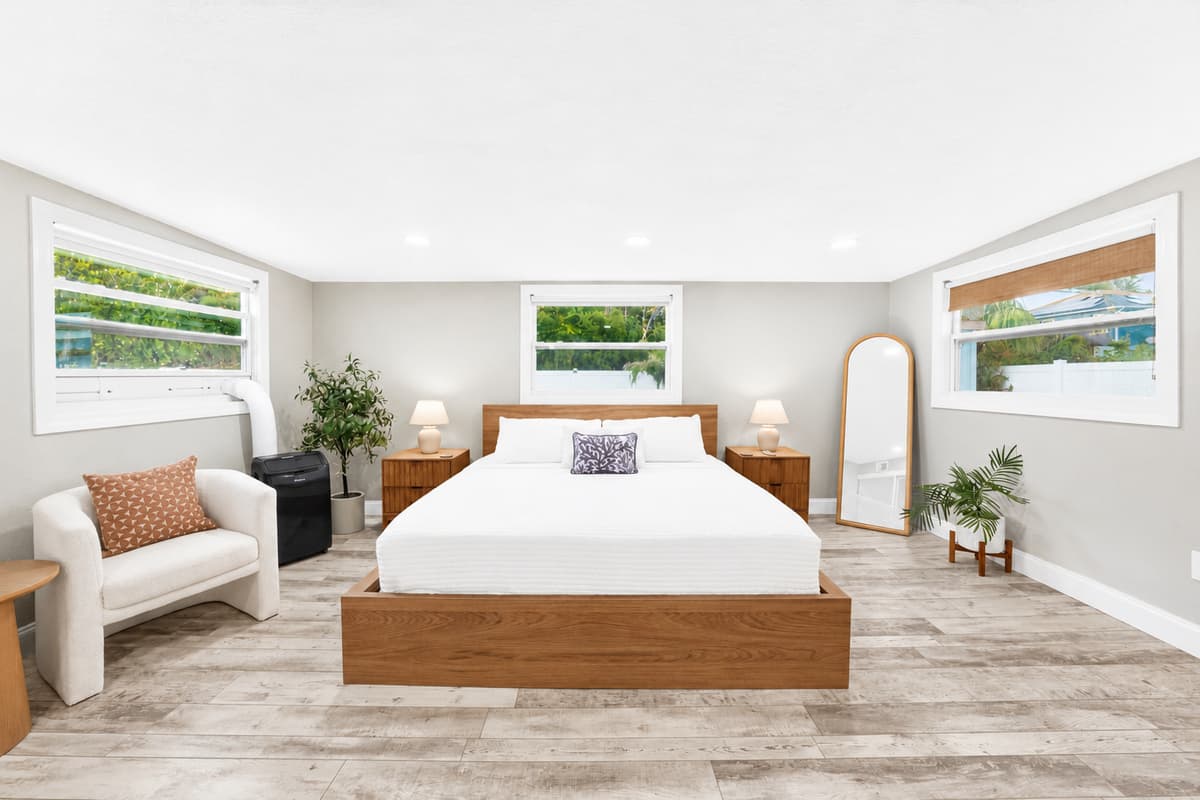 Bright bedroom retreat featuring a platform bed, cozy accent chair, large windows, and contemporary coastal décor.