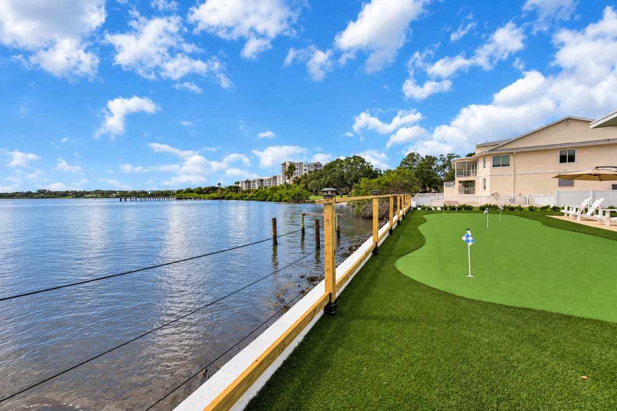 A putting green at the water's edge. Flags on the green, the bay just past the rail and condos on the far shore. Sink a putt, then sit back and watch the water.