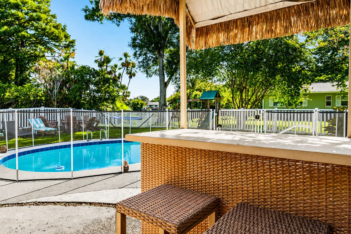 Bar under the tiki roof, pool beyond the fence, shade all afternoon. The spot everyone drifts back to.