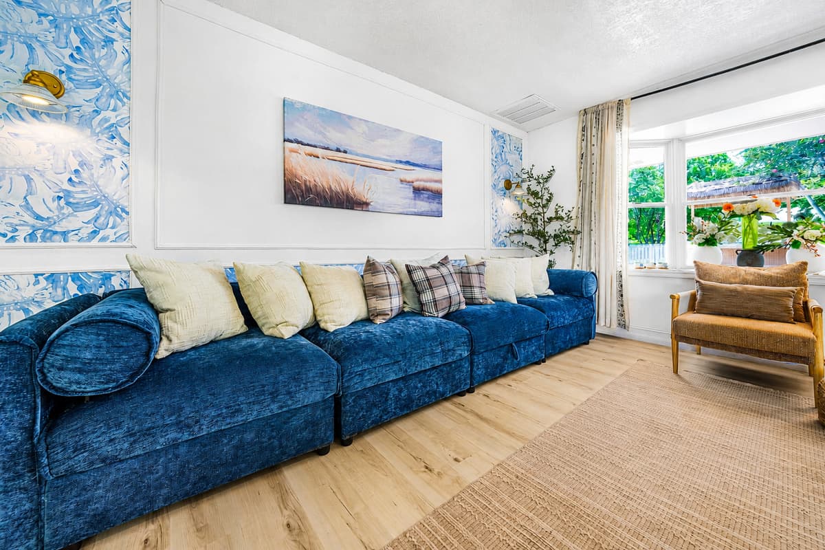 One sofa long enough for the whole family to line up on it. Ceiling fan on, curtains open, afternoon handled.
