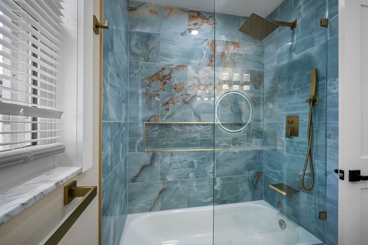Experience pure elegance in this spa-inspired bathroom featuring sleek marble tiles, a rainfall shower, and luxurious gold fixtures that radiate sophistication.