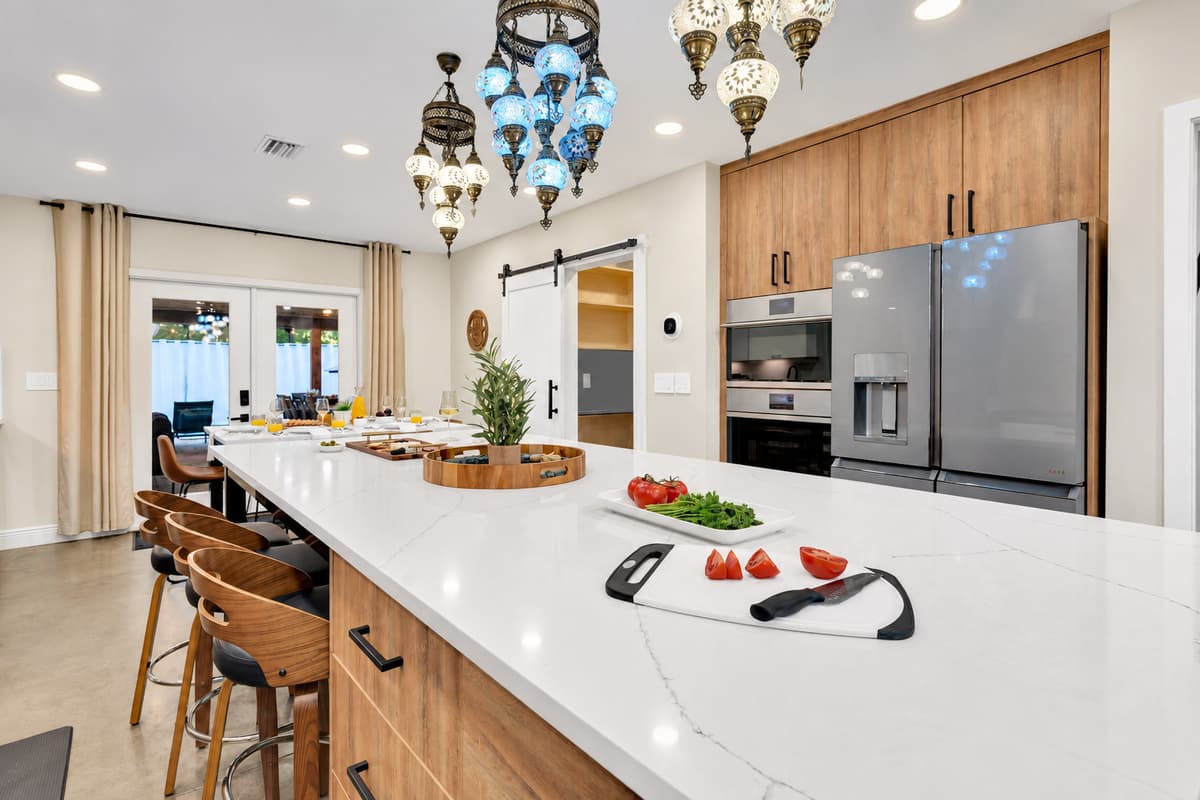 Pull up a stool and watch dinner happen. Enormous quartz island with counter seating, statement lighting and full-size appliances behind — the room the whole group ends up in every evening.