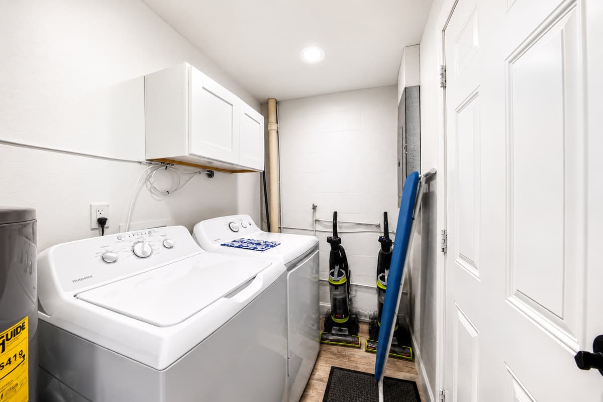 Dedicated laundry room equipped with a full-size washer and dryer, storage cabinets, and cleaning essentials.