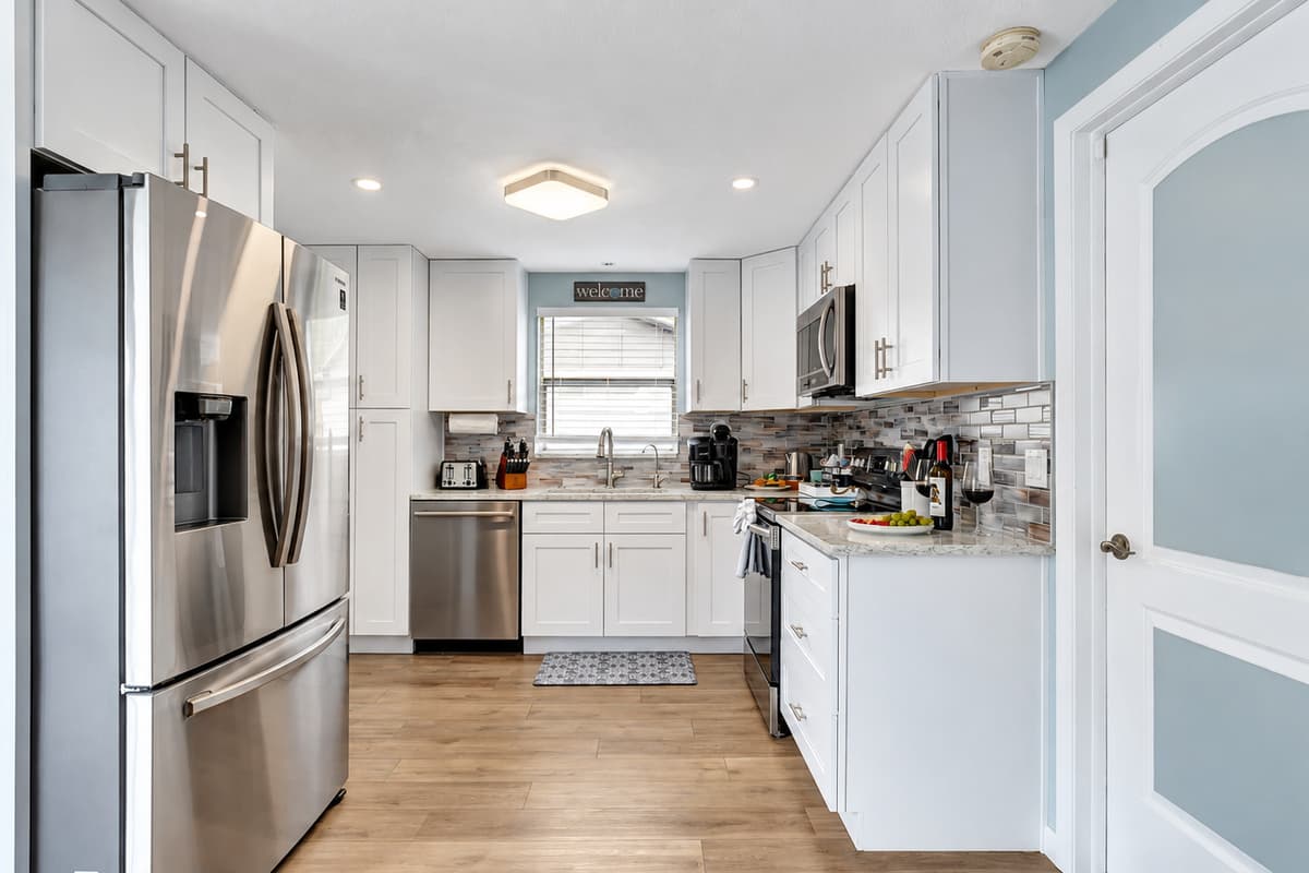 Immaculate white cupboards adorn the walls, complemented by the sleek sophistication of black and stainless finish appliances.