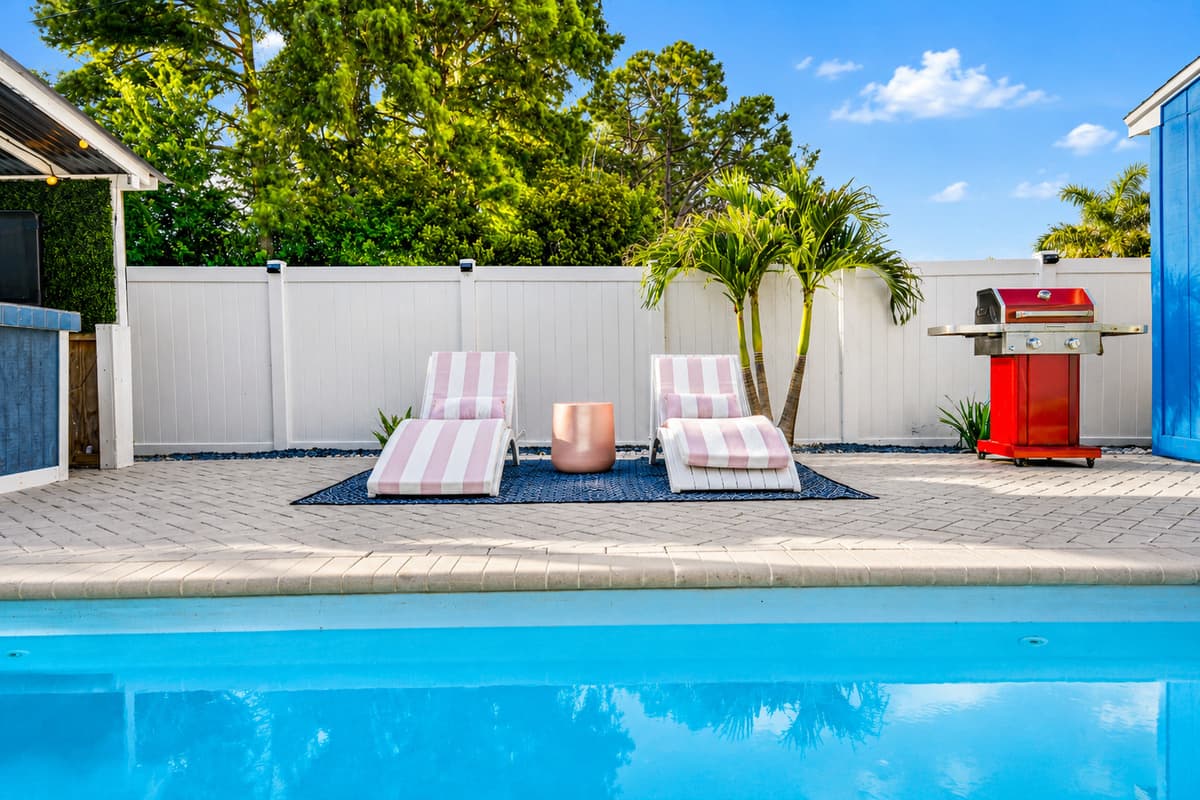 Poolside relaxation area with cushioned loungers, privacy fencing, and a built-in barbecue grill.