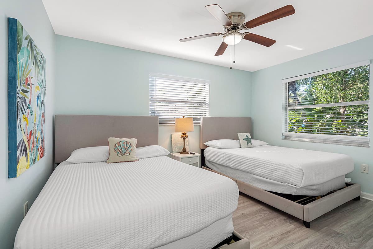 The room’s layout is both functional and inviting, offering plenty of space to relax and unwind. A nightstand with soft lighting sits between the beds.