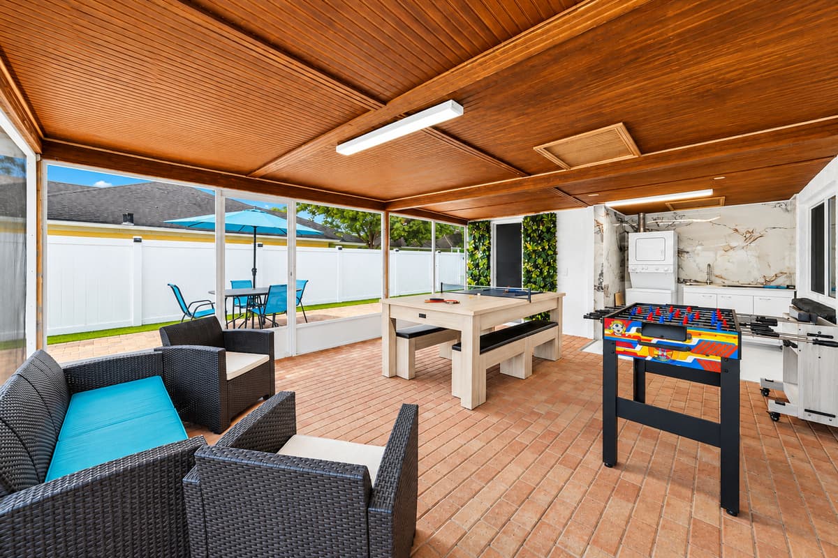 Covered outdoor entertainment area featuring comfortable seating, a pool table, foosball table, and plenty of space for family fun and relaxation.