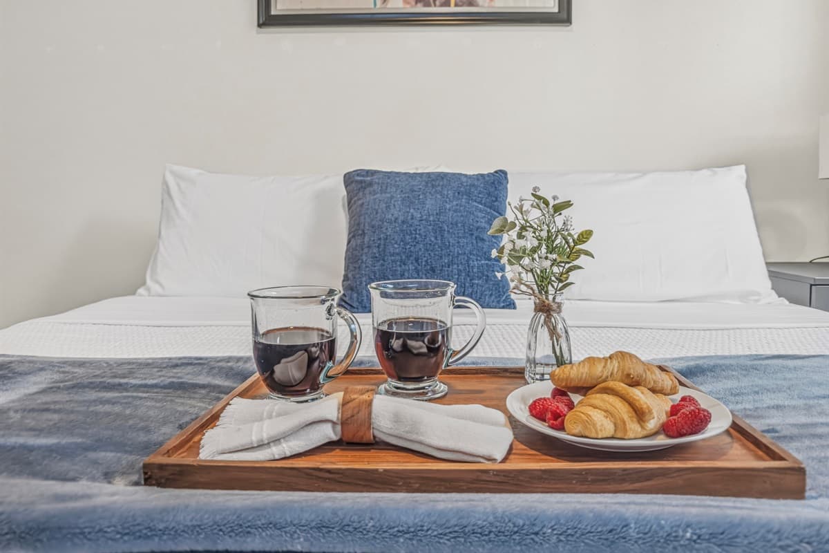 Breakfast in bed, elevated — fresh croissants, a bowl of strawberries, black coffee, and a tiny potted plant on a wooden tray. This brand-new Seminole Heights home is your personal boutique hotel experience in Tampa.