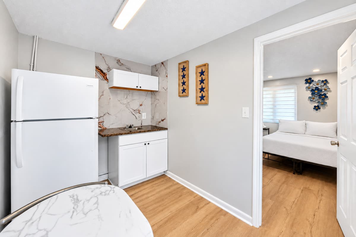 Studio suite kitchenette area featuring a refrigerator, sink, cabinets, and dining table for two, perfect for added convenience and independence.