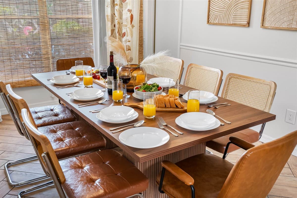 A tasteful blend of comfort and style, this dining area showcases chic mid-century seating and a bold wooden table, all beneath a designer light fixture. Perfect for casual dining or special occasions.