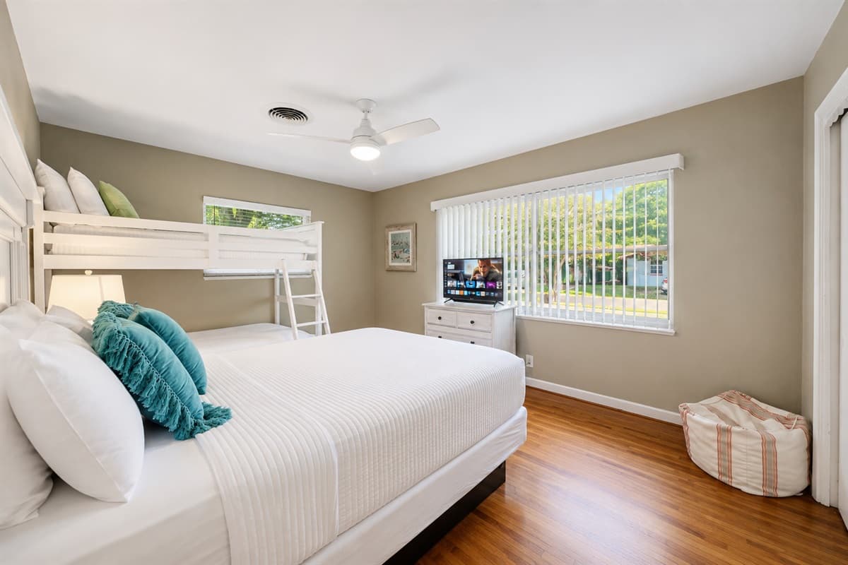 Spacious guest bedroom with comfortable sleeping arrangements, TV, and large windows overlooking the yard.