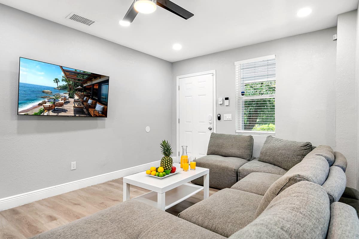 Living room with wall-mounted flat-screen TV, natural light, and modern ceiling fan.