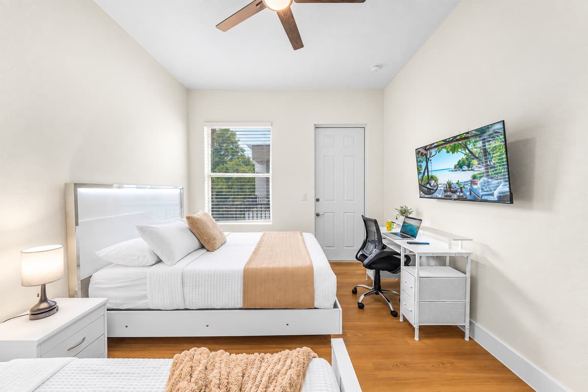 Bright bedroom with TV, workspace, and comfortable bedding.
