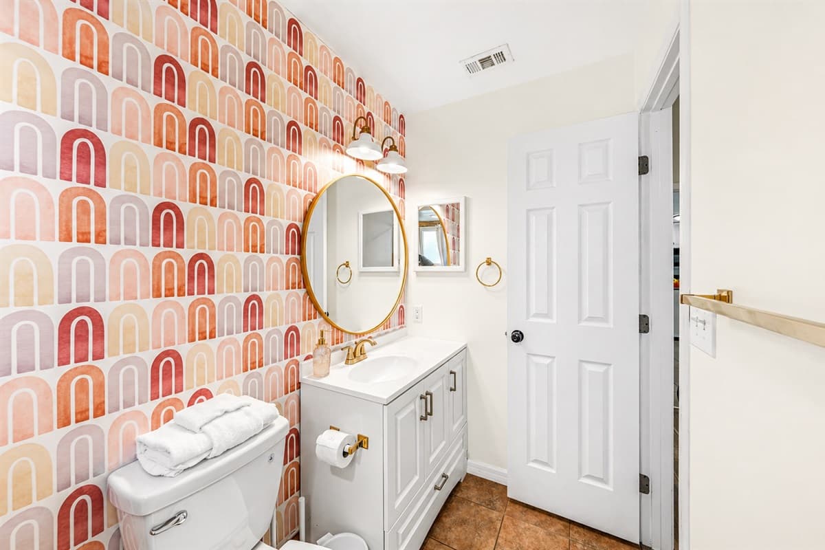 Stylish full bathroom featuring a modern vanity, gold accents, and eye-catching patterned wallpaper for a fun, upscale touch.