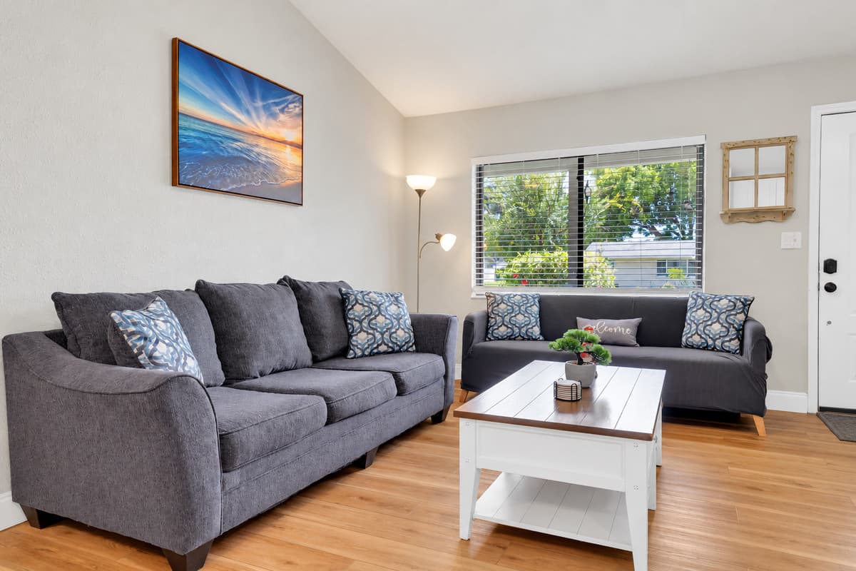 Real daylight, not lamp light: the window over the sofa keeps this room bright all afternoon, which is why the group ends up here between the beach and the pool instead of scattering to separate bedrooms.