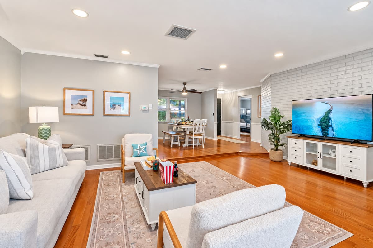 Stretch out and unwind in this spacious living area featuring warm wood floors, serene tones, and comfy furniture perfect for family time or movie night.