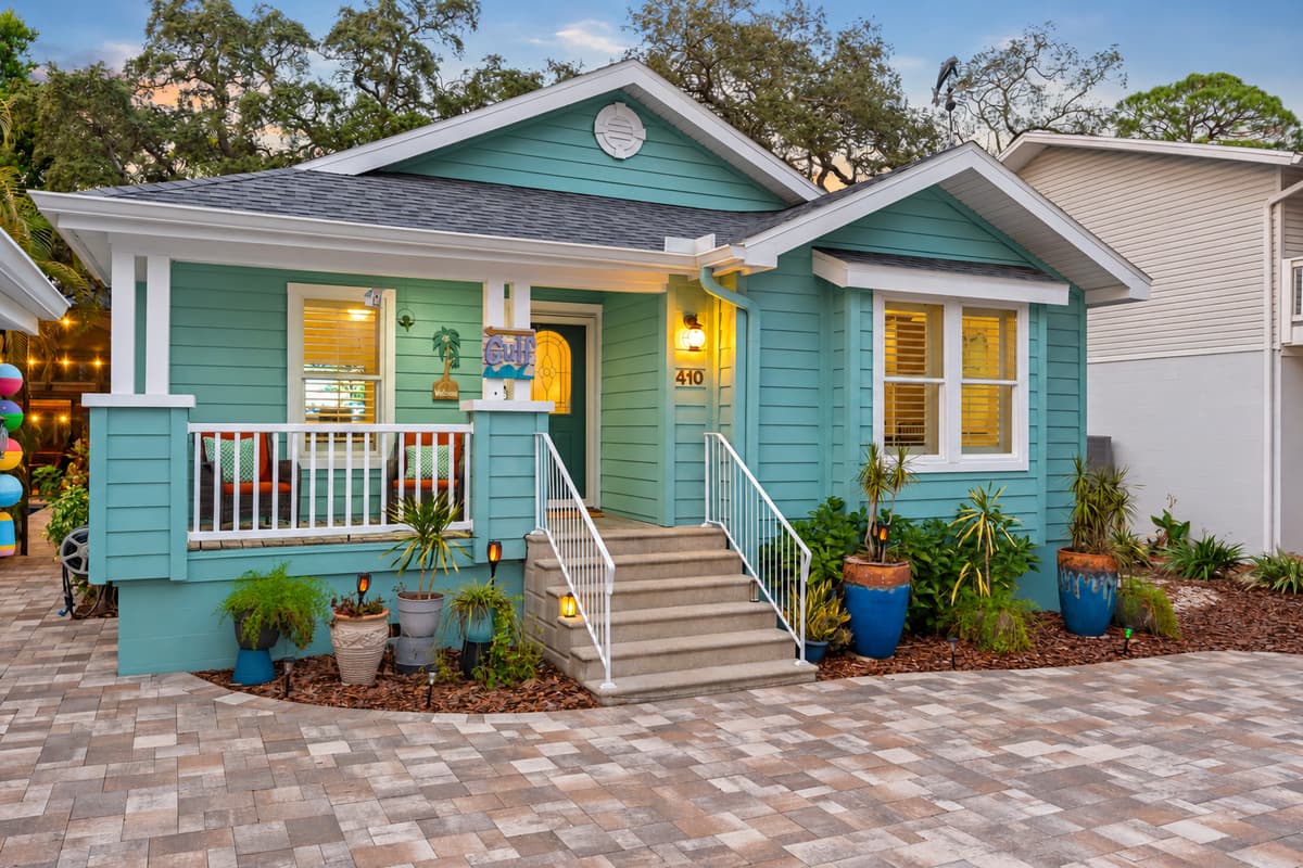 The home’s exterior radiates charm with its pastel hues, curated plants, and inviting steps leading to the front door.