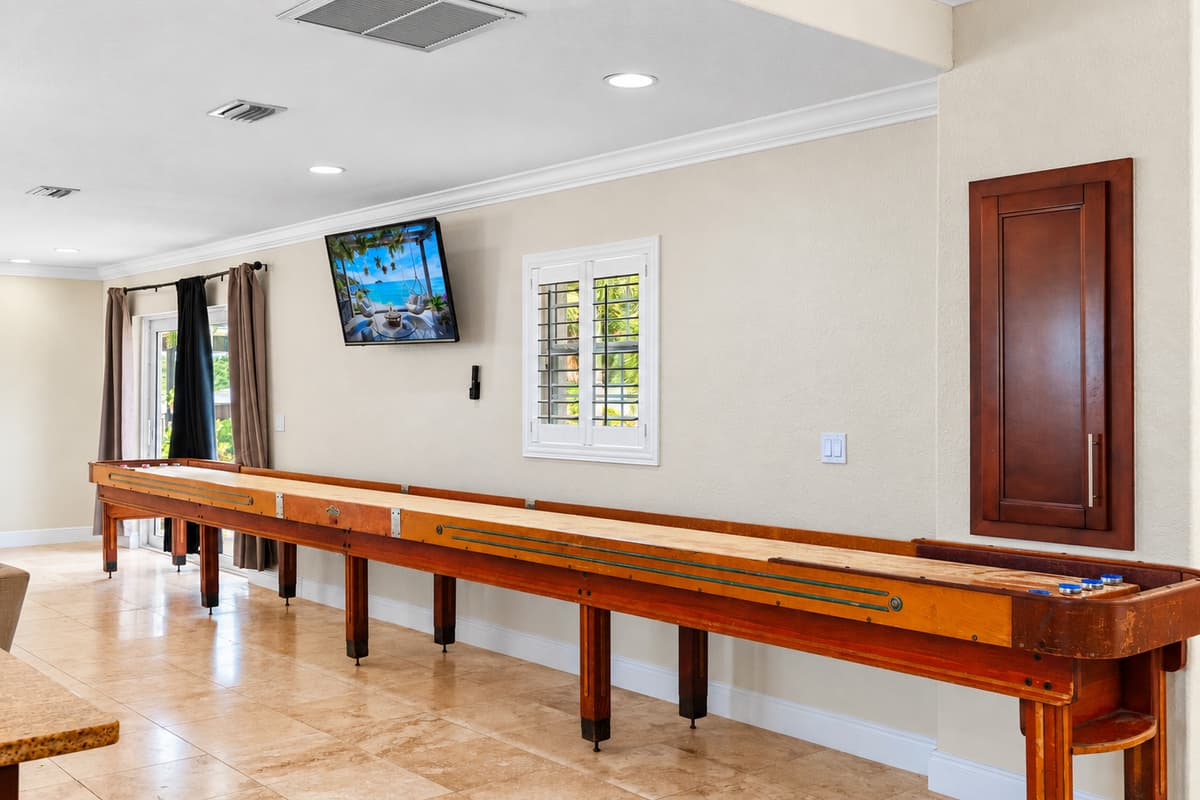 A full-length shuffleboard table lines the wall beneath a mounted flat-screen TV, perfect for game nights.