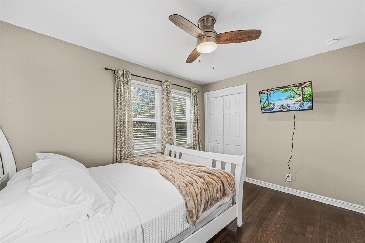 Bright bedroom featuring a comfy bed, wall-mounted TV, and large windows for a relaxing retreat.
