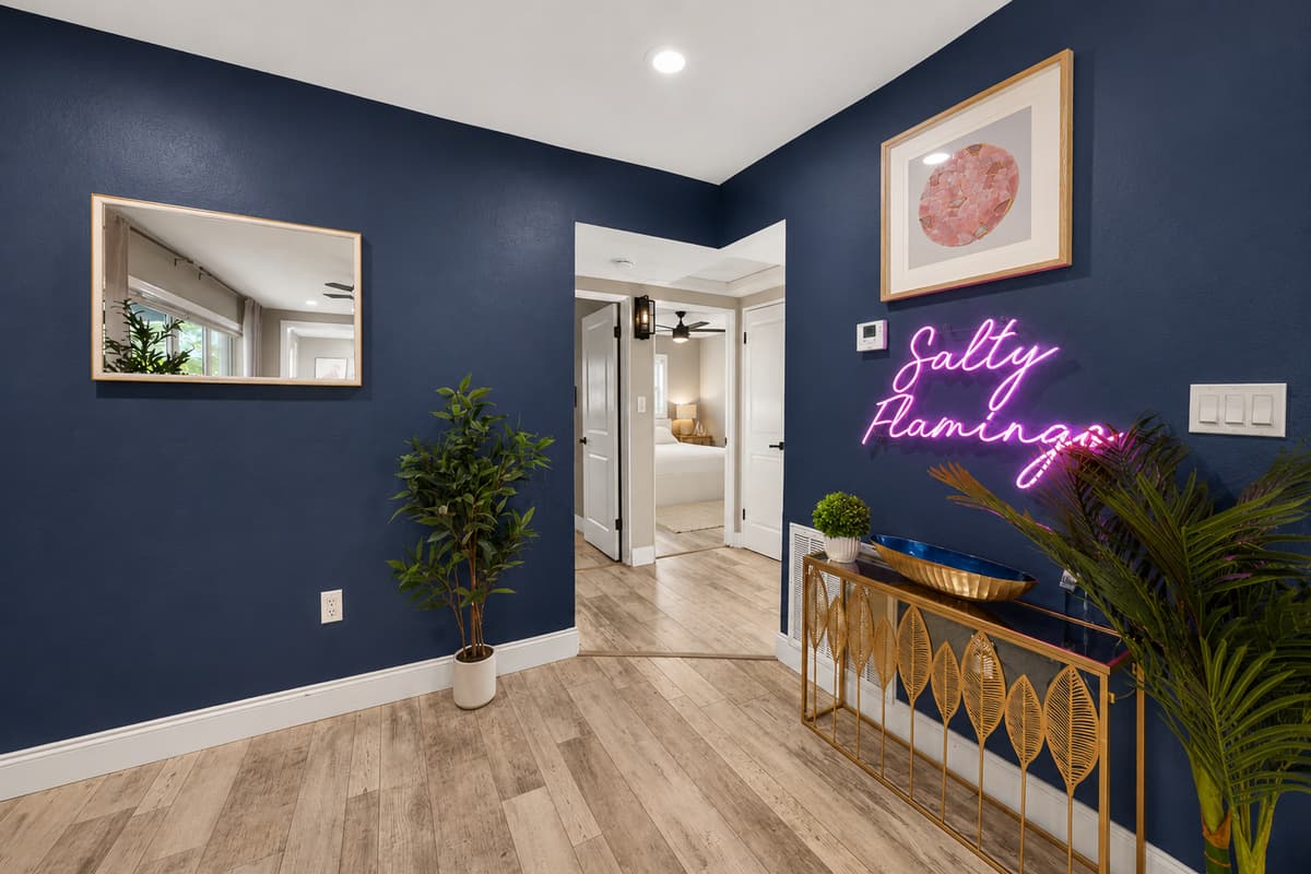 Stylish entryway with a navy accent wall, decorative console table, tropical plants, and illuminated "Salty Flamingo" neon sign.