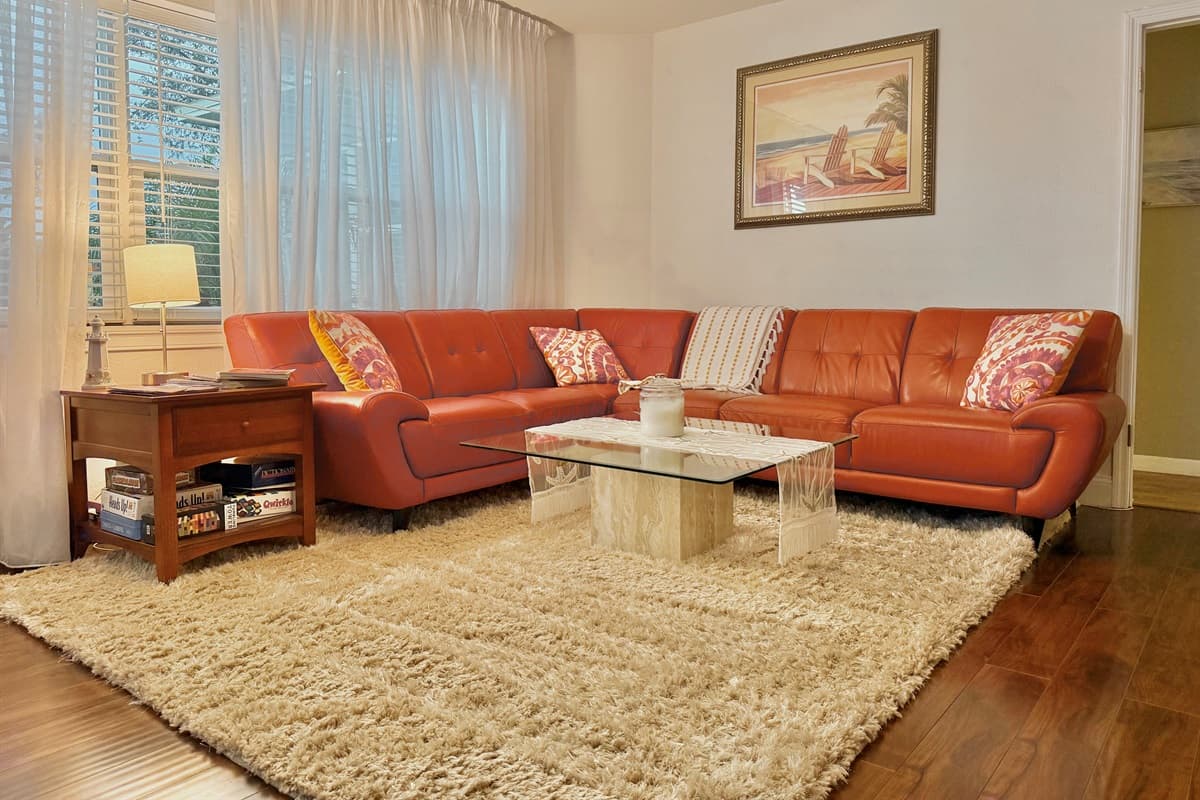 Kick back on the plush leather sectional surrounded by soft textures, coastal art, and natural light streaming through sheer curtains.