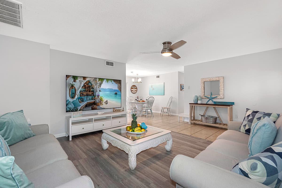 At the heart of the living area is a large, ultra-comfortable couch, adorned with decorative pillows that feature soft, beachy tones and playful coastal motifs, adding a touch of seaside flair.
