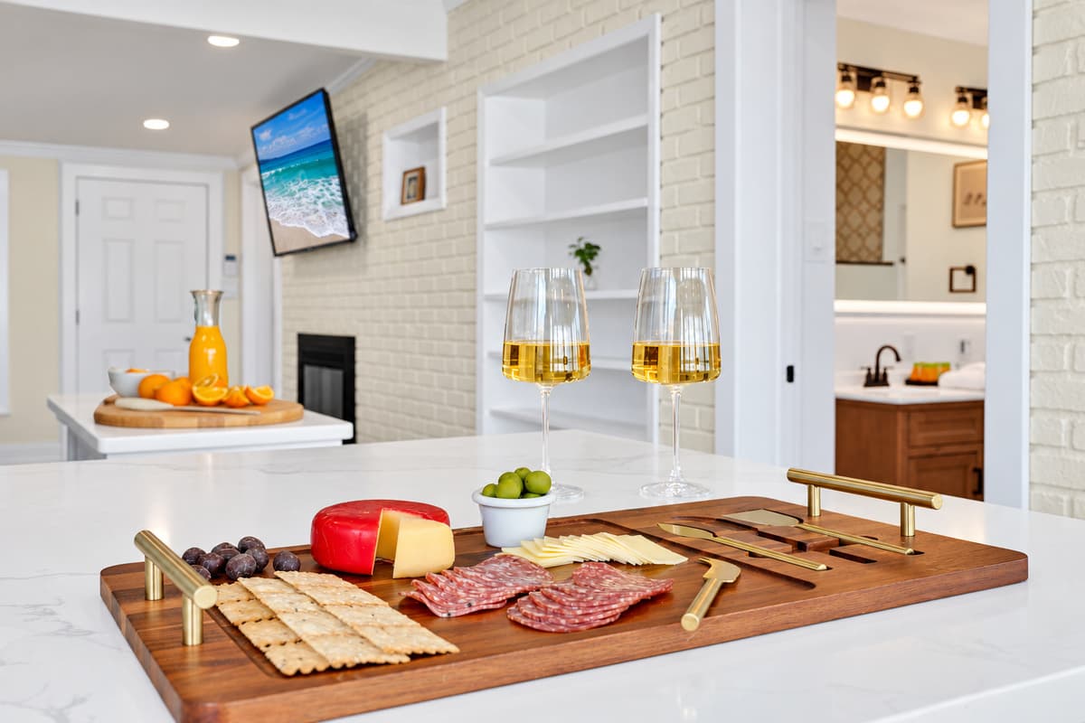 Charcuterie and wine by the fireplace. A cheese board, wine glasses and the den fireplace behind. A cozy evening without leaving the house.