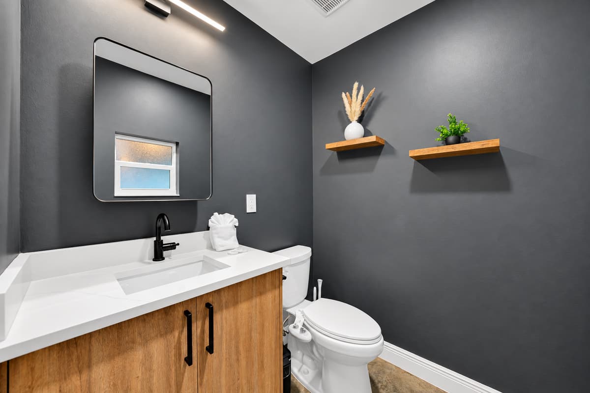 Powder room for guests, so bedrooms stay private. Floating vanity, lit mirror and dark walls — a proper half bath for the crowd, without anyone walking through someone's suite.