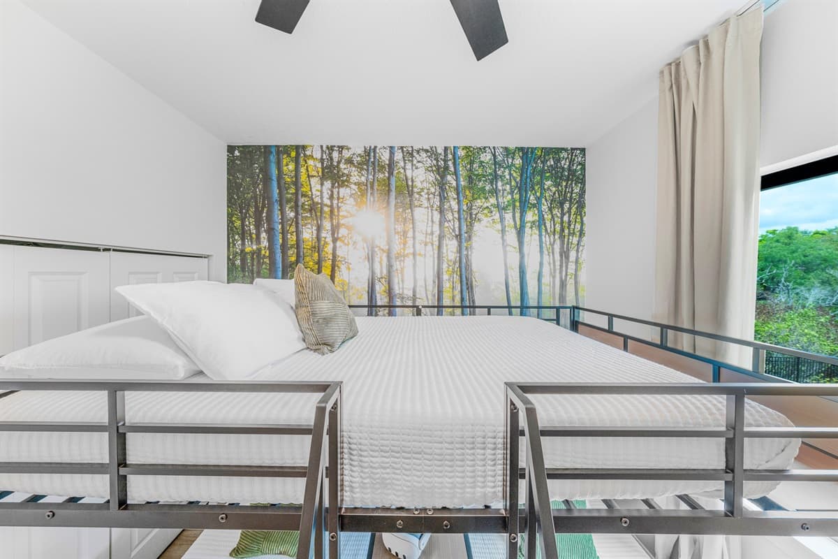 Top bunk perspective highlighting the forest-themed accent wall and bright, airy design.