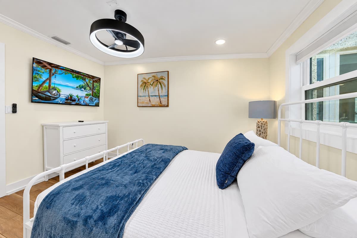 A queen room that feels like the beach. Blue bedding, palm art, a TV and a dresser. A bright, beachy room for easy sleep.